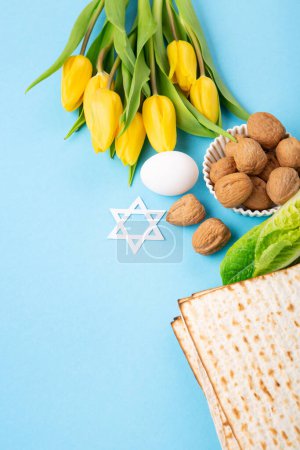 Téléchargez les photos : Carte de vœux de Pâques juive concept avec matzah matzoh (pain de vacances juif), noix, fleurs de tulipes jaunes sur table bleue. Seder Pessah printemps fond de vacances, espace de copie. - en image libre de droit