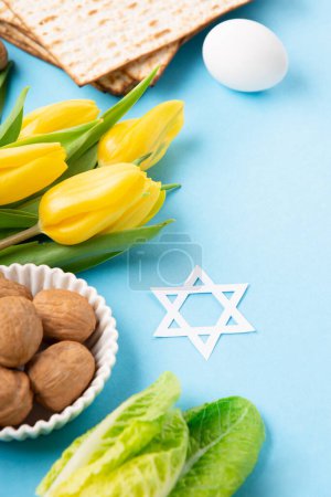 Photo for Jewish holiday Passover greeting card concept with matzah matzoh (jewish holiday bread), walnuts, yellow tulip flowers on blue table. Seder Pesach spring holiday background, copy space. - Royalty Free Image