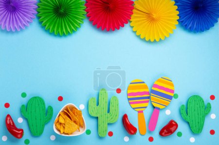 Téléchargez les photos : Fête d'arrière-plan mexicain avec des copeaux de nachos mexicains traditionnels, piment rouge, cactus et maracas sur fond bleu. Cinco de Mayo (Cinquième mai) concept de célébration. Vue du dessus, espace de copie. - en image libre de droit