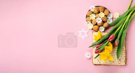 Téléchargez les photos : Jewish holiday Passover greeting card concept with matzah, Star of David, spring yellow daffodil, tulips, daisy flowers, walnuts on pink table. Seder Pesach spring holiday background, copy space. - en image libre de droit