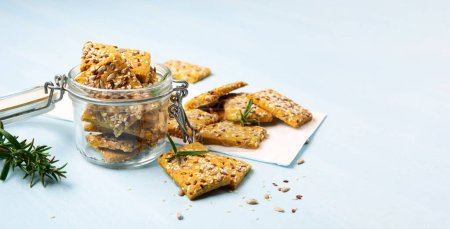 Photo for Gluten free Homemade Crackers and rosemary on Blue background. Healthy eating, ancient grain food, dieting, balanced food concept. Cereals gluten-free, millet, quinoa, flax seeds, sunflower seeds. - Royalty Free Image