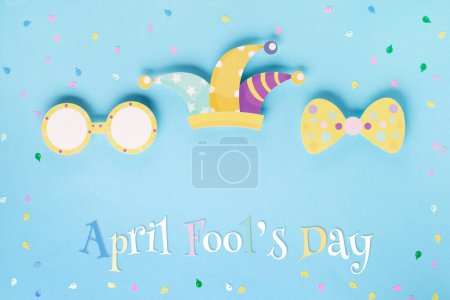 Foto de Tarjeta de vacaciones del día del tonto de abril con sombrero de bufón, confeti y gafas divertidas sobre fondo azul, vista superior. Día Internacional de la risa. Concepto para tarjetas de felicitación, banners, volantes. - Imagen libre de derechos
