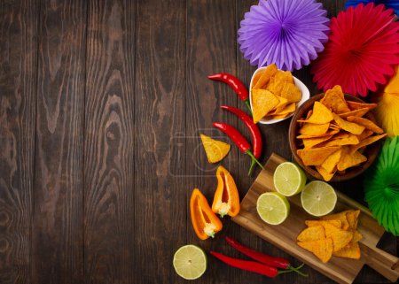 Photo for Cinco de Mayo (Fifth of May) celebration concept. Mexican background fiesta with Traditional Mexican nachos chips, red chili peppers, green lime on dark wooden background. Top view, copy space. - Royalty Free Image