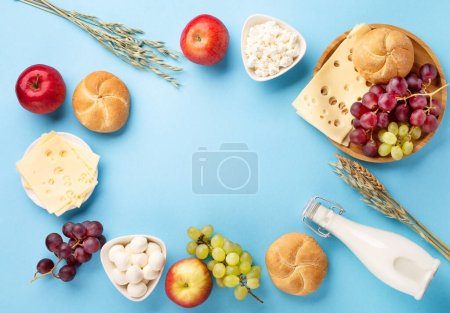 Foto de Happy Shavuot festive card, Jewish religious holiday concept. Dairy products, fruits, cheese, bread, milk bottle on blue background. Flat lay, top view, copy space. - Imagen libre de derechos