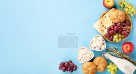 Téléchargez les photos : Carte festive Happy Shavuot, concept de fête religieuse juive. Produits laitiers, fruits, fromage, pain, bouteille de lait sur fond bleu. Pose plate, vue du dessus, espace de copie. - en image libre de droit