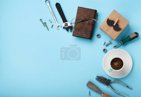 Photo for Fathers day holiday card concept with craft gift box, black moustache, cup of coffee, tools, book and glasses on blue background, top view, copy space. - Royalty Free Image