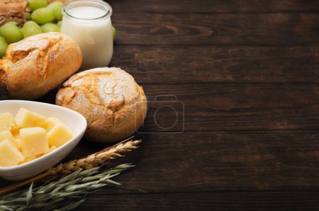 Photo for Happy Shavuot festive card. Jewish religious holiday concept. Dairy products, fruits, cheese, bread, milk bottle, cottage cheese, wheat on dark wooden background. Top view, copy space. - Royalty Free Image