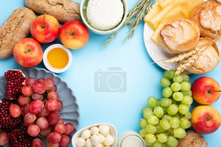Photo for Happy Shavuot festive card. Jewish religious holiday concept. Dairy products, grapes, cheese, bread, milk, cottage cheese, wheat, honey on blue background. Top view, copy space. - Royalty Free Image