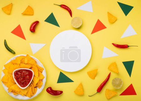 Téléchargez les photos : Fond de la fiesta mexicaine avec des copeaux de nachos mexicains traditionnels, des piments et de la sauce à la salsa de tomate sur fond jaune. Cinco de Mayo (Cinquième mai) concept de célébration. Vue du dessus, espace de copie. - en image libre de droit