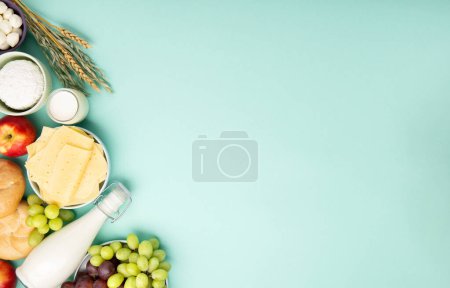 Photo for Happy Shavuot festive card. Jewish religious holiday concept. Dairy products, fruits, cheese, bread, milk bottle, cottage cheese, wheat on blue mint background. Top view, copy space. - Royalty Free Image
