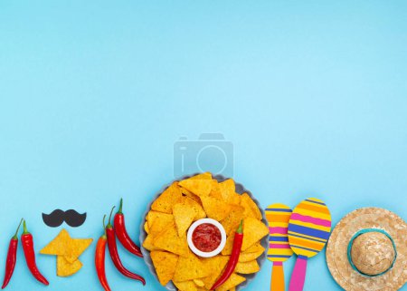Téléchargez les photos : Fond de la fête mexicaine avec des copeaux de nachos mexicains traditionnels, des piments et de la sauce à la salsa de tomate sur la table bleue. Cinco de Mayo (Cinquième mai) concept de célébration. Vue du dessus, espace de copie. - en image libre de droit