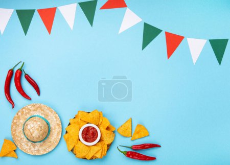 Téléchargez les photos : Fond de la fête mexicaine avec des copeaux de nachos mexicains traditionnels, des piments et de la sauce à la salsa de tomate sur la table bleue. Cinco de Mayo (Cinquième mai) concept de célébration. Vue du dessus, espace de copie. - en image libre de droit