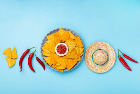 Photo for Mexican fiesta background with Traditional Mexican nachos chips, chilli peppers and tomato salsa sauce on blue table. Cinco de Mayo (Fifth of May) celebration concept. Top view, copy space. - Royalty Free Image