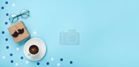 Téléchargez les photos : Fathers day holiday card concept with craft gift box, moustache noire, tasse de café et verres sur fond bleu, vue de dessus, espace de copie. - en image libre de droit