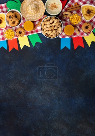 Foto de Festa Junina Summer Festival Concepto de carnaval. Sombrero de paja brasileño, tortas de maíz, cacahuetes y banderas de colores sobre fondo azul madera, vista superior. Diseño para tarjeta de felicitación, invitación o cartel de vacaciones - Imagen libre de derechos