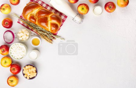 Téléchargez les photos : Joyeux Shavuot carte festive. Concept de fête religieuse juive. Produits laitiers, pommes fraîches, fromage, pain, lait, fromage cottage, blé et miel sur fond blanc. Vue du dessus, espace de copie. - en image libre de droit