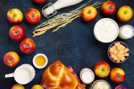 Photo for Happy Shavuot festive card. Jewish religious holiday concept. Dairy products, fresh apples, cheese, bread, milk, cottage cheese, wheat and honey on dark blue wooden background. Top view, copy space. - Royalty Free Image