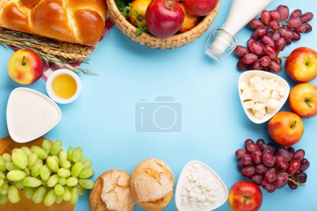 Photo for Happy Shavuot festive card. Jewish religious holiday concept. Dairy products, fresh apples, grapes, cheese, bread, milk, cottage cheese, wheat and honey on blue background. Top view, copy space. - Royalty Free Image
