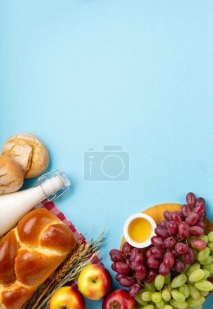 Téléchargez les photos : Joyeux Shavuot carte festive. Concept de fête religieuse juive. Produits laitiers, pommes fraîches, raisins, fromage, pain, lait, fromage cottage, blé et miel sur fond bleu. Vue du dessus, espace de copie. - en image libre de droit