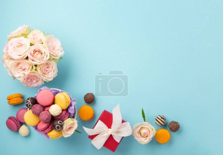 Téléchargez les photos : Biscuits sucrés macarons, boîte cadeau rouge, fleurs roses et bonbons au chocolat sur fond bleu. Le printemps présente le concept pour la fête des mères, la fête des femmes, l'anniversaire. Pose plate, espace vide pour le texte ou le message - en image libre de droit