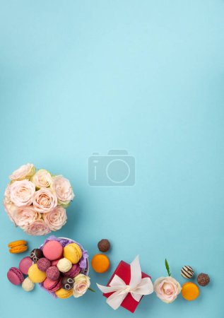 Photo for Sweet cookies macaroons, red gift box, rose flowers and chocolate candies on blue background. Spring presents concept for Mothers day, womans day, birthday. Flat lay, empty space for text or message - Royalty Free Image
