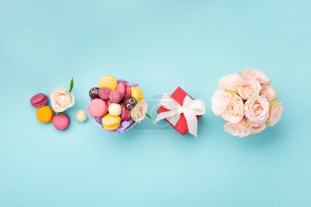 Photo for Sweet cookies macaroons, red gift box, rose flowers and chocolate candies on blue background. Spring presents concept for Mothers day, womans day, birthday. Top view, empty space for text - Royalty Free Image