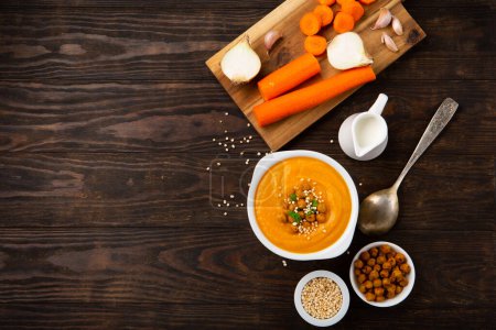 Photo for Autumn Vegetarian pumpkin and carrot cream soup with chickpeas and herbs on dark wooden background. Comfort food, fall and winter healthy slow food concept. - Royalty Free Image