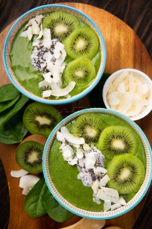 Photo for Green smoothie bowl with organic Spinach, Banana, Chia Seeds, fresh kiwi on dark wooden background. Vegan, Food and drink, healthy dieting and nutrition, alkaline, vegetarian concept. - Royalty Free Image