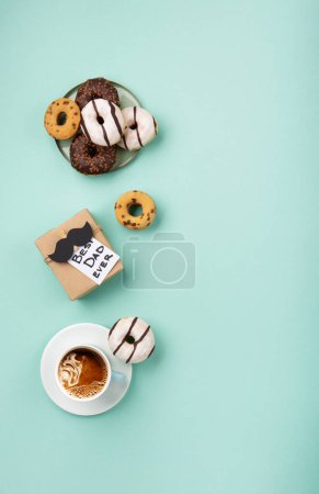 Photo for Fathers day holiday card concept with craft gift box, black moustache, cup of coffee and donuts or doughnuts on blue mint background, top view, copy space. - Royalty Free Image