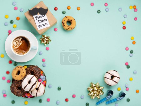Téléchargez les photos : Fathers day holiday card concept with craft gift box, moustache noire, tasse de café et beignets ou beignets sur fond bleu menthe, vue de dessus, espace de copie. - en image libre de droit
