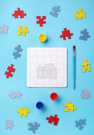 Téléchargez les photos : Journée de la fierté autistique ou concept de Journée mondiale de sensibilisation à l'autisme. Puzzles, symbole de sensibilisation au trouble du spectre autistique et peintures colorées sur fond bleu. Vue du dessus, espace de copie. - en image libre de droit