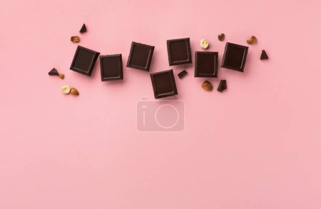 Téléchargez les photos : World Chocolate Day, july 07.  Dark chocolate bar pieces with nuts on pink background, top view, copy space. Holiday greeting card or banner concept. - en image libre de droit