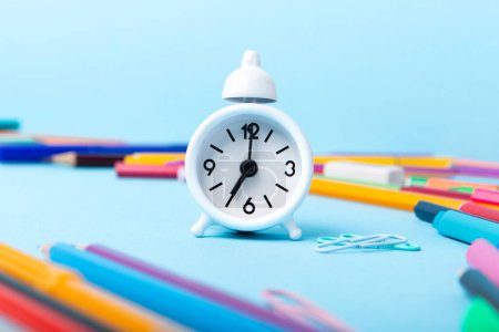 Photo for Back to school, Exam, Education concept on blue background. School scattered stationery, notepads, pens, pencils, paper clips and white alarm clock on blue table, copy space. - Royalty Free Image