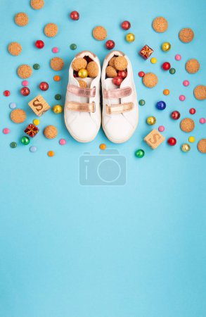 Photo for Saint Nicholas Day, 6 December. Christmas card with children's shoes, sweets, candy, gingerbread cookies, gifts on blue table. Traditional Sinterklaas, Saint Nicholas day background, winter holiday in Germany and Western Europe. - Royalty Free Image
