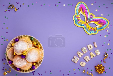 Foto de Mardi Gras King Cake doughnuts or donuts, masquerade festival carnival mask, gold beads and golden, green confetti on purple background. Holiday party invitation, greeting card concept. - Imagen libre de derechos