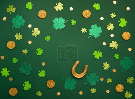 Téléchargez les photos : Carte de jour St Patricks avec symboles traditionnels pour fête irlandaise. Fer à cheval doré, pièces d'or, feuilles de trèfle, trèfles verts sur fond vert. Vue de dessus. Concept de célébration de la Saint-Patrick. - en image libre de droit