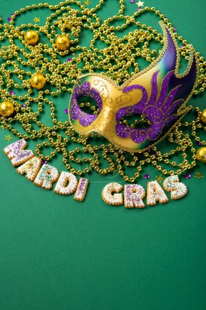 Téléchargez les photos : Mardi Gras King Cake cookies, masquerade festival carnival mask, gold beads and golden, green, purple confetti on green background. Holiday party invitation, greeting card concept. - en image libre de droit