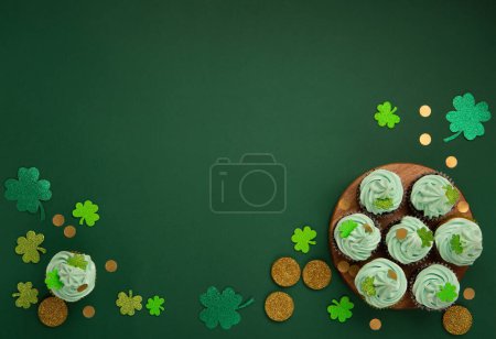 Photo for St. Patrick's Day vanilla and chocolate cupcakes with green frosting and  shiny clover decorations on green paper background. Irish holiday dessert concept. Top view, copy space. - Royalty Free Image