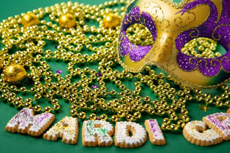 Téléchargez les photos : Mascarade du festival Mardi Gras masque de carnaval, biscuits King Cake, perles d'or et confettis dorés, verts, violets sur fond vert. Invitation de fête, concept de carte de voeux. - en image libre de droit