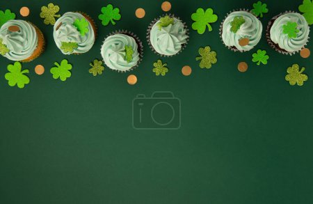 Téléchargez les photos : Gâteaux à la vanille et au chocolat Saint-Patrick avec glaçage vert et décorations trèfle brillant sur fond de papier vert. Dessert irlandais de vacances concept. Vue du dessus, espace de copie. - en image libre de droit