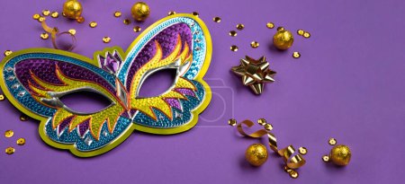 Photo for Mardi Gras or Purim masquerade festival carnival mask, sweet chocolate candies, gold beads, golden confetti on purple background. Holiday party invitation, greeting card concept, copy space - Royalty Free Image