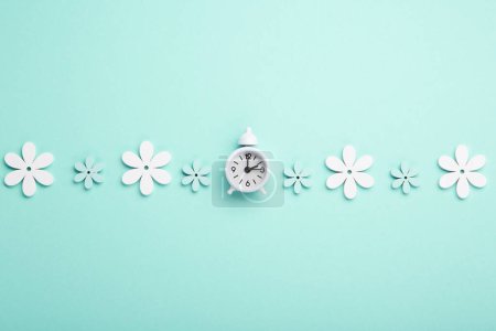 Foto de White alarm clock and Daisy Flowers on blue mint background. Spring forward, Time Change, Daylight Saving Time Ends, Changing the time on the watch to spring time, Summer back concept. - Imagen libre de derechos