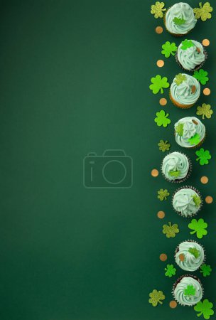 Foto de Día de San Patricio cupcakes de vainilla y chocolate con glaseado verde y decoraciones de trébol brillante sobre fondo de papel verde. Concepto de postre navideño irlandés. Vista superior, espacio de copia. - Imagen libre de derechos