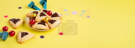 Téléchargez les photos : Biscuits hamantaschen trempés au chocolat, masque de carnaval, bruyant, bonbons sucrés et décor de fête sur fond jaune. Pourim célébration juive concept de vacances. - en image libre de droit