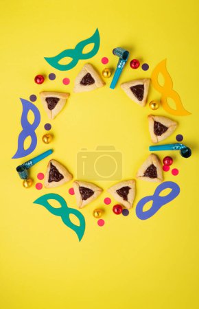 Photo for Chocolate dipped hamantaschen cookies, Carnival mask, noisemaker, sweet candies and festive party decor on yellow background, Top view. Purim celebration jewish holiday concept. - Royalty Free Image