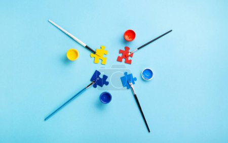Photo for World Autism Awareness Day or month concept. Creative design for April 2. Puzzles, symbol of awareness for autism spectrum disorder and colorful paints on blue background. Top view, copy space. - Royalty Free Image