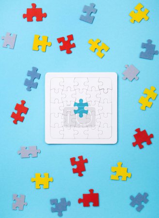 Téléchargez les photos : Journée de la fierté autistique, concept de Journée mondiale de sensibilisation à l'autisme. Puzzle blanc, symbole de sensibilisation au trouble du spectre autistique et détails colorés sur fond bleu. Vue du dessus, espace de copie. - en image libre de droit