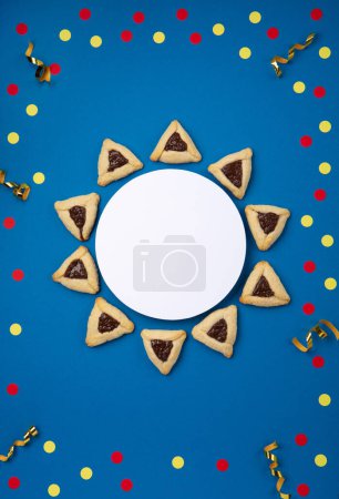 Téléchargez les photos : Chocolat maison biscuits hamantaschen Pourim, pâtisserie triangulaire et décor festif de fête de carnaval sur fond bleu foncé, vue sur le dessus. Pourim célébration juive concept de vacances. - en image libre de droit