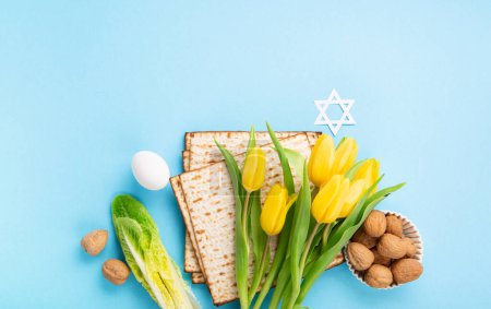 Téléchargez les photos : Carte de vœux de Pâques juive concept avec matzah matzoh (pain de vacances juif), noix, fleurs de tulipes jaunes sur table bleue. Seder Pessah printemps arrière-plan, espace de copie. - en image libre de droit
