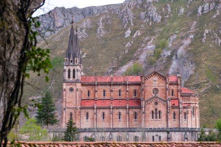 Foto de Una estructura alta situada en Covadonga, Asturias, con un gran edificio con un campanario que se eleva por encima. La arquitectura emana un sentido de significación histórica y reverencia religiosa. - Imagen libre de derechos